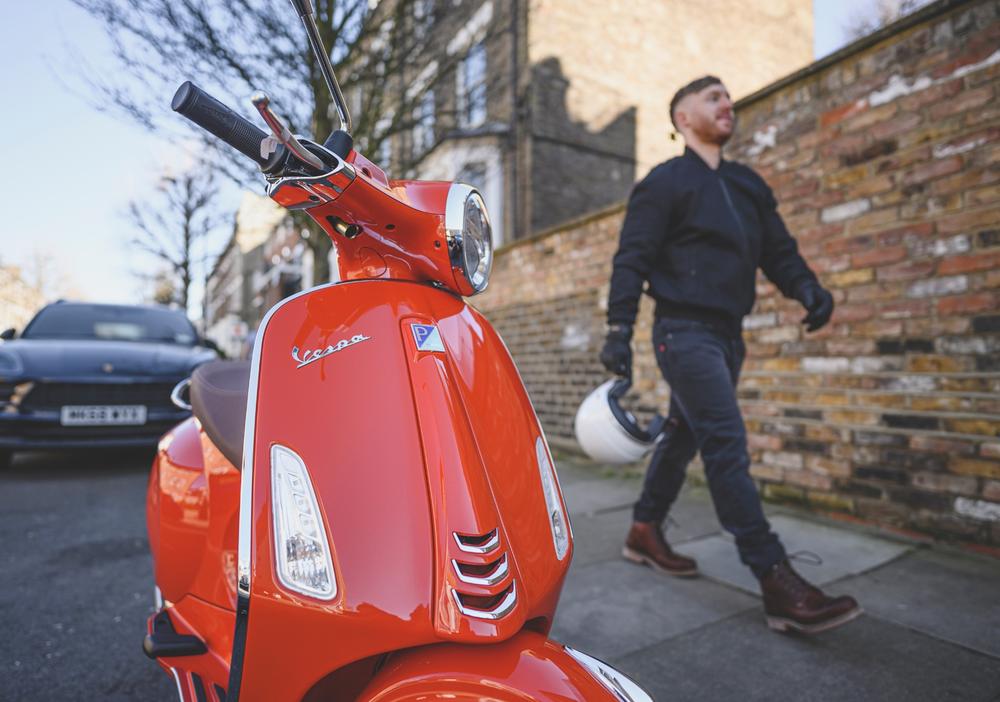 A man walking with confidence knowing his classic/retro red Vespa GTS 300 HPE E5 is insured with Lexham