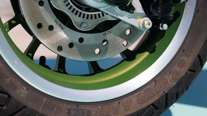 Close-up view of a motorcycle's wheel assembly, showcasing a green-spoked rim, metallic brake disc, and suspension components.