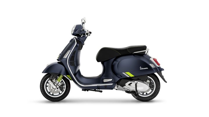 A blue Vespa scooter with green accents is displayed from a side view, showcasing its sleek design and chrome details.