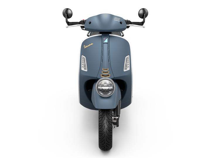 A front view of a vintage-style blue Vespa scooter, featuring a round headlight, black mirrors, and a sleek body design.