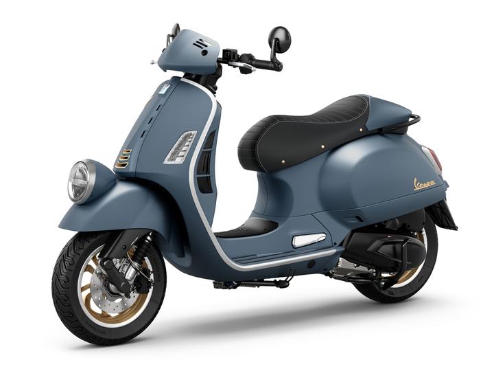 A stylish blue scooter with a retro design, featuring a round headlight, black seat with gold accents, and gold-rimmed wheels.