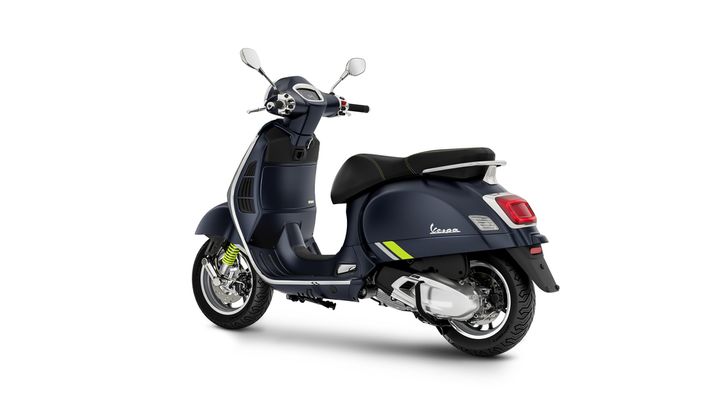 A dark blue Vespa scooter with a sleek design, featuring a black seat, distinctive green stripes, and chrome accents, positioned at a slight angle to showcase its rear profile.