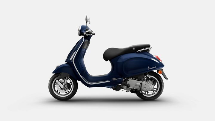 A navy blue Vespa scooter displayed from the side, featuring a sleek design, chrome accents, and a comfortable black seat.