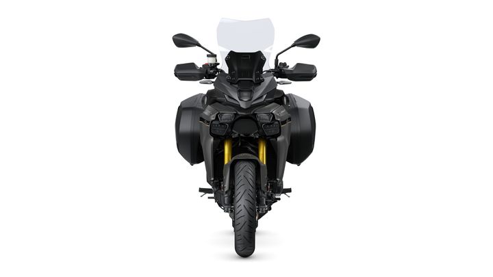 A front view of a modern motorcycle with a sleek design, featuring wide side bags, a tall windshield, and a prominent headlamp. The bike showcases a two-tone finish with black and metallic elements, as well as a thick front tire and visible suspension components.