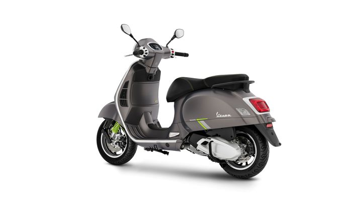 A sleek gray Vespa scooter shown from a slightly elevated angle, highlighting its modern design, saddle, and rear wheel with a distinctive green shock absorber.