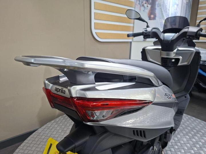 Close-up of a rearview of a silver Aprilia scooter, highlighting its sleek tail section and integrated taillights.