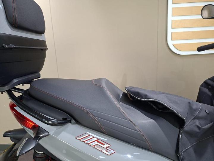 Close-up view of a motorcycle seat with a black and gray color scheme, featuring red stitching and a backrest, displayed against a neutral background.