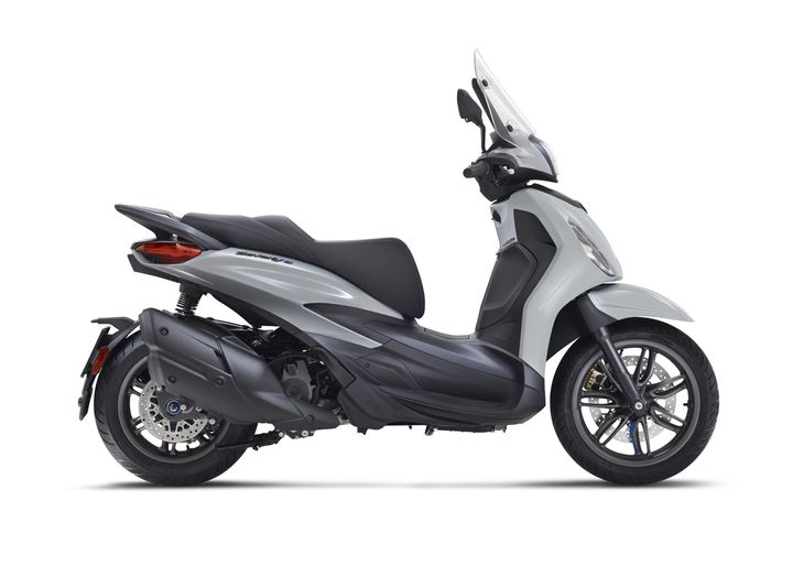 A sleek, modern scooter in silver and gray, featuring a streamlined body, a comfortable seat, and a tall windscreen, displayed from the side against a white background.