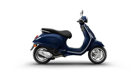 A sleek blue scooter with a comfortable black seat, showcasing a chrome-plated exhaust and stylish wheels, positioned on a white background.
