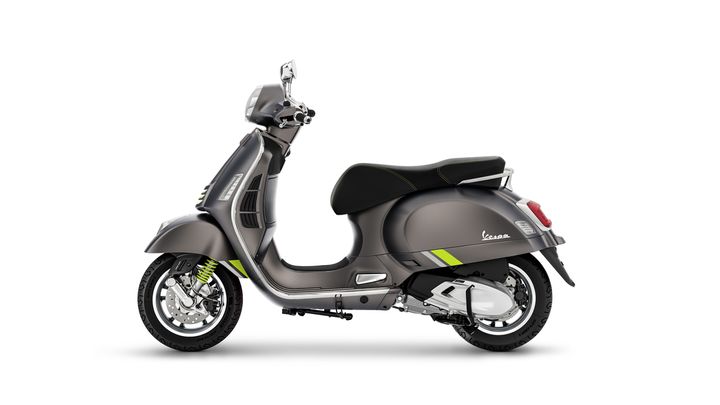A grey Vespa scooter featuring green accents, viewed from the side with a sleek, retro design.