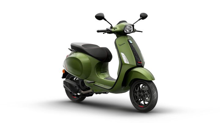 A green Vespa scooter with a black seat and red accents, positioned at a slight angle against a white background.