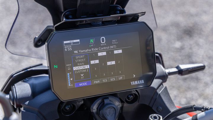 A close-up of a motorcycle's LCD display showing the Yamaha Ride Control interface, indicating the ride mode options (Sport, Street, Rain, Custom 1, Custom 2) and current settings, with digital readouts for speed and trip details.