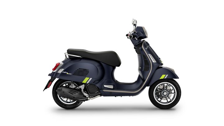 Vespa GTS 125 SuperTech Euro 5+ A sleek, modern scooter in a dark blue finish with green accents, featuring a stylish design, comfortable seat, and intricate wheel detail, captured from a side perspective.