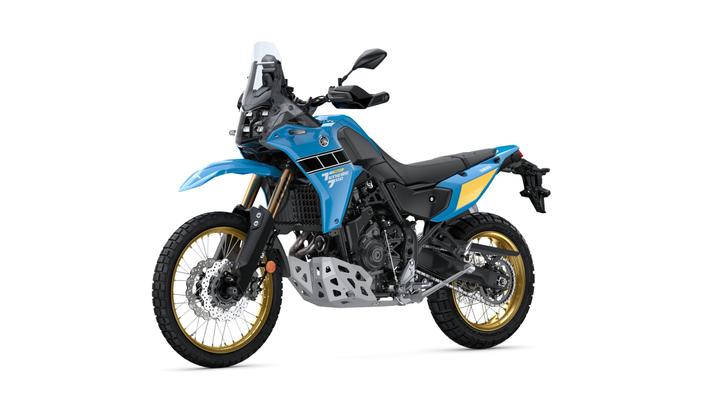 A blue and black adventure motorcycle with a silver skid plate and gold wheels, positioned at a slight angle, showcasing its rugged design and modern features.