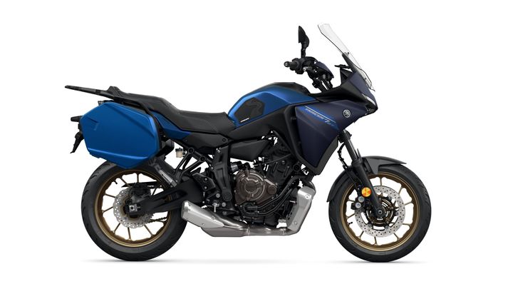A blue Yamaha motorcycle, model Tracer 7 GT, is displayed from the side view. The bike features a sleek design with a black seat, gold-accented wheels, and a large blue side pannier.