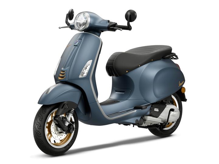 A blue vintage-style scooter with a sleek design, featuring a rounded front, silver accents, and a black seat with horizontal stripes, displayed at a slight angle.