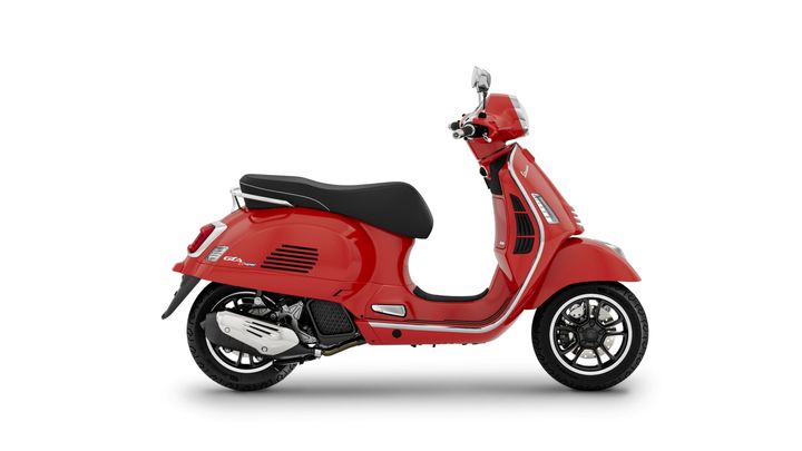 A side view of a red Vespa scooter with a sleek design, featuring a black seat and chrome accents.