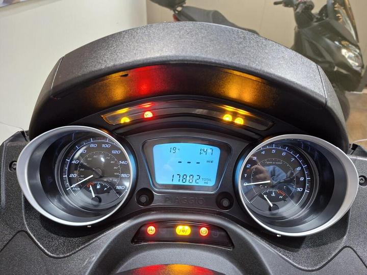 A close-up view of a scooter's dashboard displaying a speedometer, tachometer, digital screen showing a total mileage of 17,882 miles, and various indicator lights.