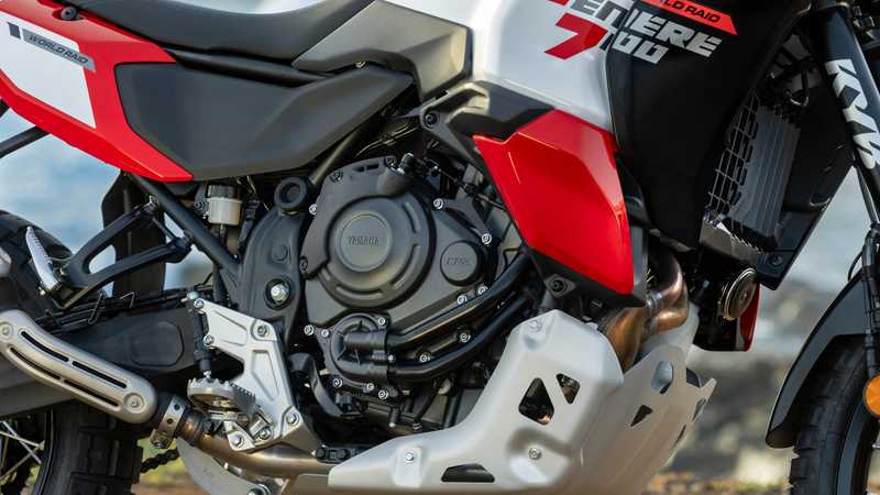 Close-up view of a motorcycle's engine, showcasing its sleek design and components in red, black, and silver colors, with a blurred background suggesting an outdoor setting.
