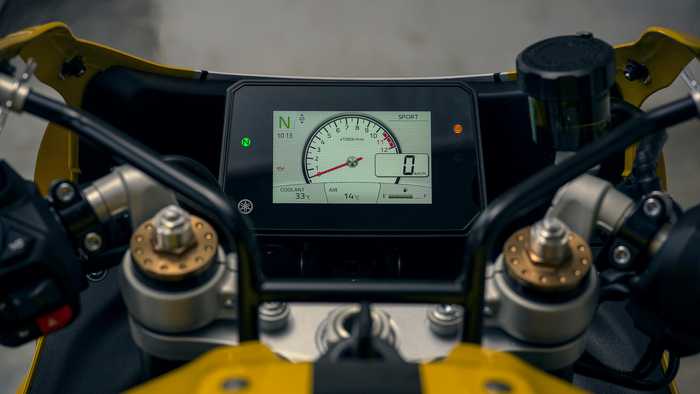 Close-up of a motorcycle's digital dashboard, displaying speed, RPM, coolant temperature, air temperature, and gear indicator, with a sport mode setting visible.