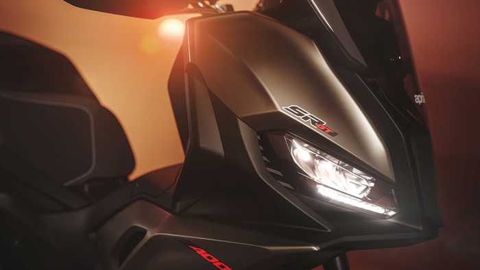 Close-up of a sleek motorcycle with a glossy black finish, featuring the model name "SR 400" prominently displayed. The design includes a tall windshield and modern headlight, with warm lighting in the background creating a dramatic ambiance.