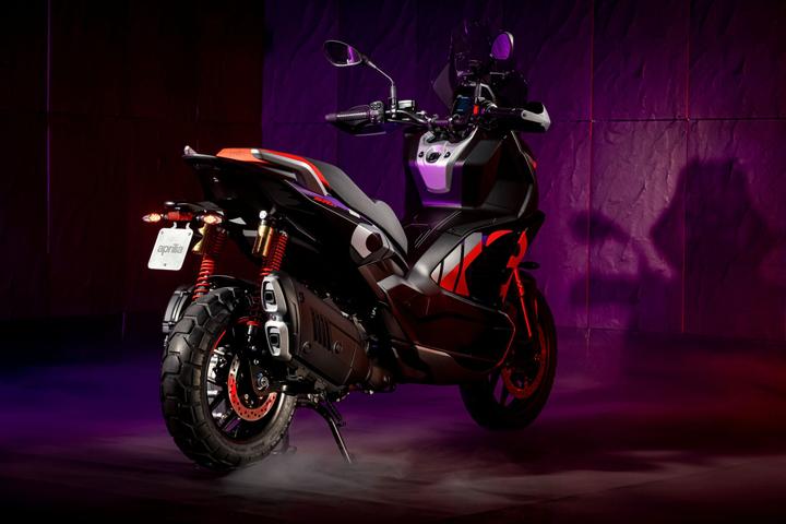 A sleek black and red scooter displayed against a gradient purple background, showcasing its modern design and details such as pronounced tires and dual exhaust pipes.