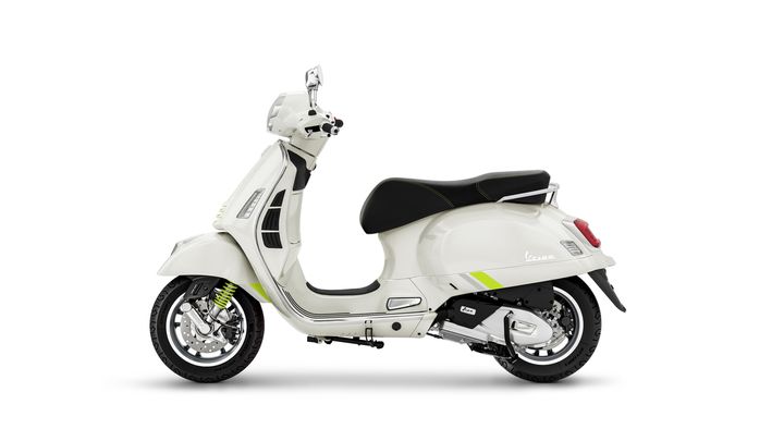 A white Vespa scooter with a sleek design, featuring a black seat and green accents, is displayed against a plain white background.