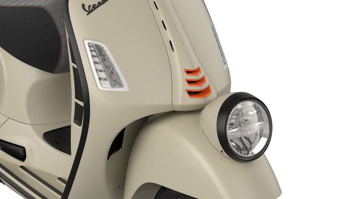 Close-up view of a beige scooter front, showcasing the headlight, orange accent details, and sleek body design.