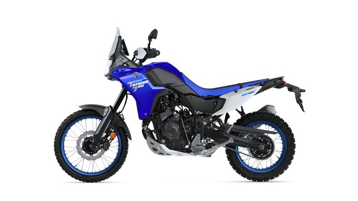 A blue and white Yamaha Tenere 700 adventure motorcycle, positioned at a slight angle to showcase its design, features knobby tires for off-road capability, a tall windshield, and a rugged frame.