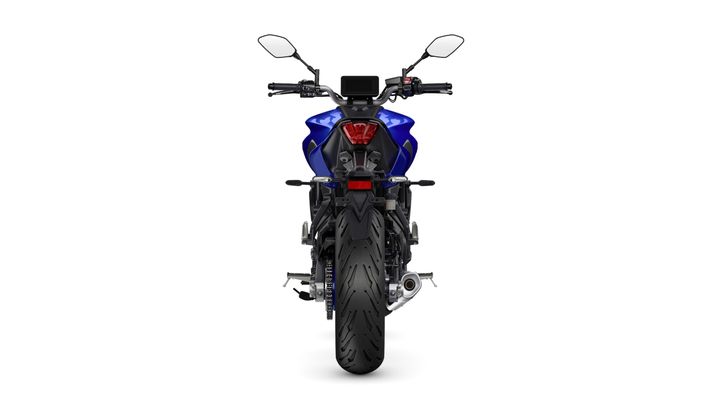 A blue motorcycle viewed from the rear, showcasing its tail light, exhaust pipe, and wide rear tire against a plain white background.