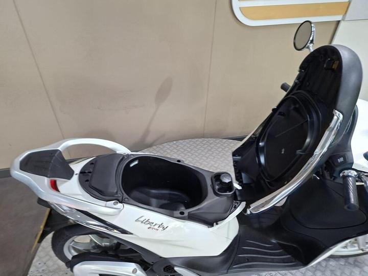 A white scooter with an open storage compartment under the seat, displaying its inner capacity and design features.