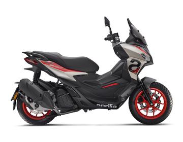 A sleek, modern scooter in gray and black with red accents, featuring a streamlined design and prominent "Aprilia" branding on the side. The scooter is shown from the side, highlighting its sporty profile, dual-tone seat, and eye-catching wheels.