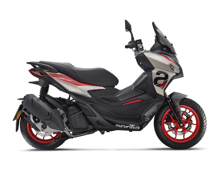 A sleek, modern scooter in gray and black with red accents, featuring a streamlined design and prominent "Aprilia" branding on the side. The scooter is shown from the side, highlighting its sporty profile, dual-tone seat, and eye-catching wheels.