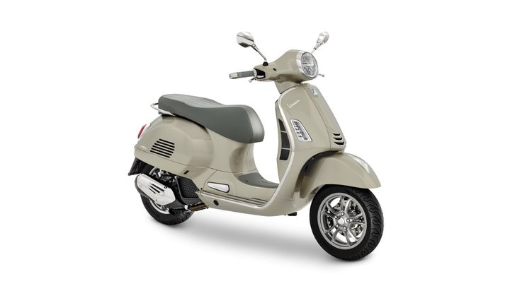 A beige Vespa scooter with a gray seat and chrome accents, positioned at an angle to showcase its design features.