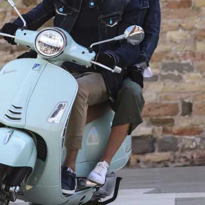 Two people riding on a light blue Vespa scooter