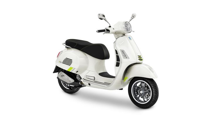 A white scooter with a black seat, featuring green accents, multi-spoke wheels, and a classic design, positioned at a slight angle.