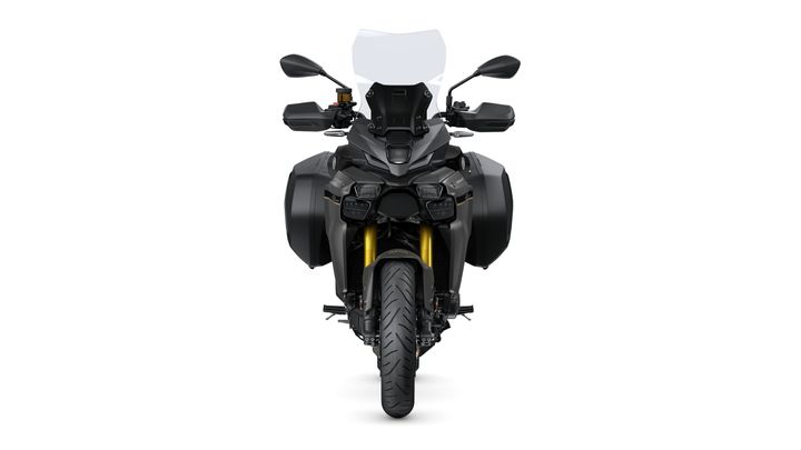 A front view of a modern motorcycle featuring a sleek design, prominent headlights, a tall windscreen, and dual side bags, with a bold tire and gold-colored suspension components.