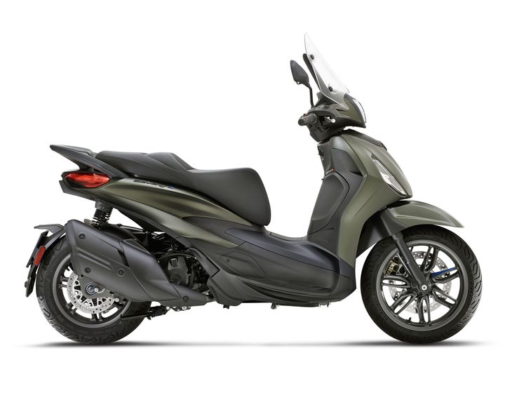 A sleek, modern scooter in a matte olive green finish, viewed from the side, showcasing its streamlined design, large front windshield, and alloy wheels.