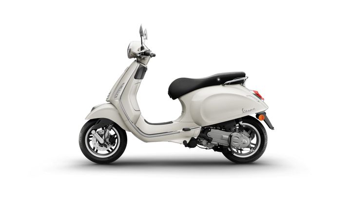A side view of a cream-colored Vespa scooter with a black seat parked on a white background.