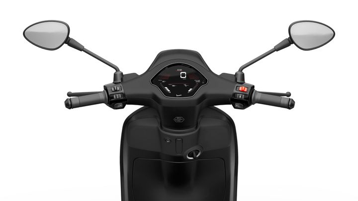A high-angle view of a scooter's handlebars, featuring two mirrors, a digital display showing speed and indicators, and controls on both sides. The design is sleek and predominantly black.