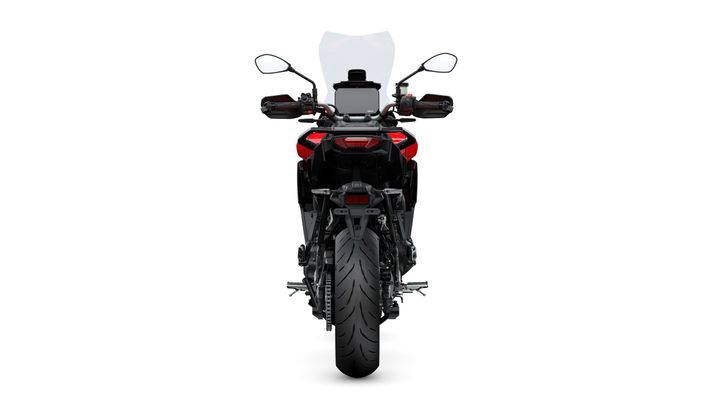 A rear view of a sleek black motorcycle with a red accent, featuring a tall windshield, handlebars with mirrors, and a wide, textured rear tire.