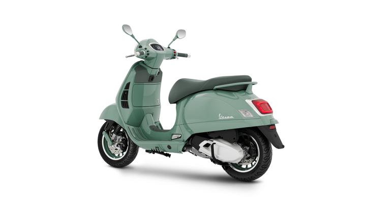 A mint green Vespa scooter, viewed from the rear-left side, showcasing its sleek design, round mirrors, and chrome accents.