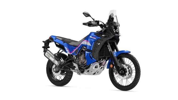 A blue Yamaha Tenere 700 motorcycle is displayed, showcasing its rugged design, front fender, and off-road tires, with a black windscreen and silver exhaust system visible.