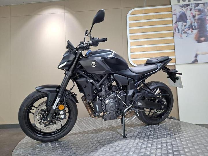 A sleek black motorcycle is displayed on a circular platform, showcasing its modern design and features, with a neutral background.