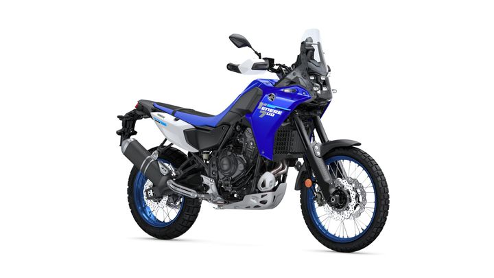 A blue and white adventure motorcycle with a rugged design, featuring wide tires, a prominent front fender, and a tall windscreen, parked on a white background.