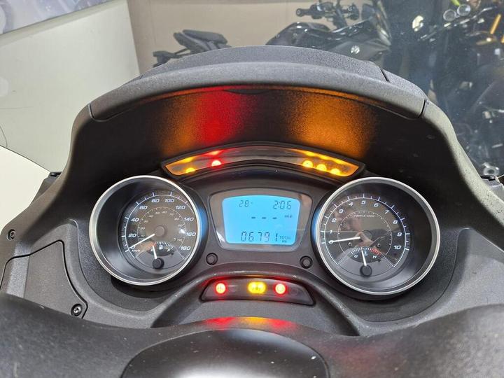 Dashboard of a motorcycle showing speedometer in km/h, tachometer in RPM, and digital display with mileage and temperature indicators. Warning lights are also visible.