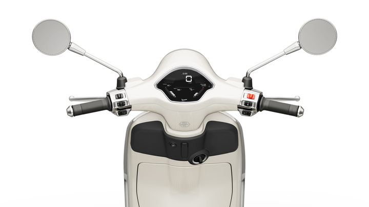 Close-up view of a scooter's handlebars, featuring two mirrors, a digital dashboard in the center displaying speed, and controls on either side, set against a plain white background.