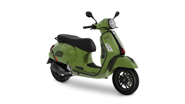 A green vintage-style scooter with a black seat and red accents, positioned at an angle to showcase its sleek design and round headlight.