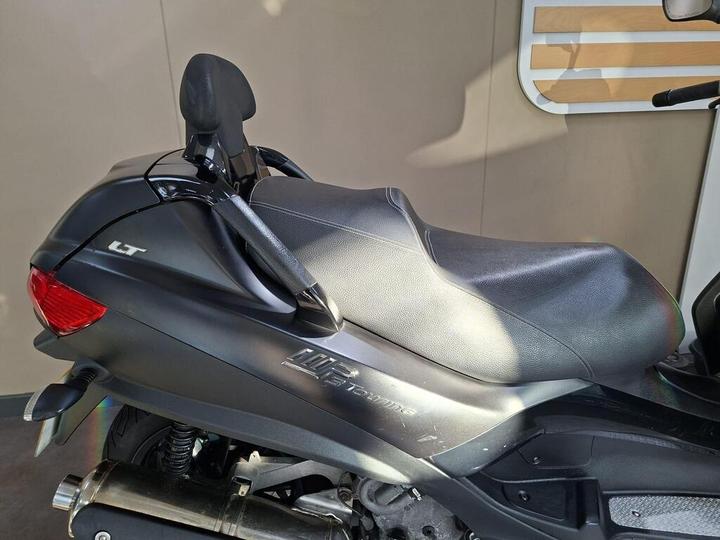 A close-up view of the rear section of a black scooter, featuring a textured seat, rear tail light, and the model designation "LT" on the side.