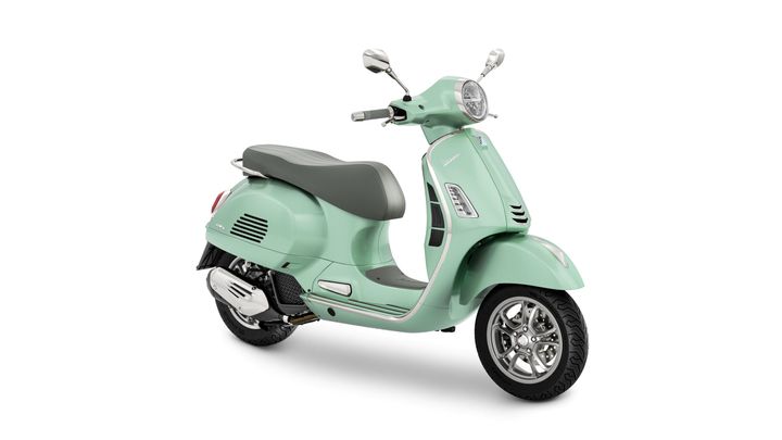 A mint green Vespa scooter with a gray seat and chrome accents, positioned slightly to the right against a white background.